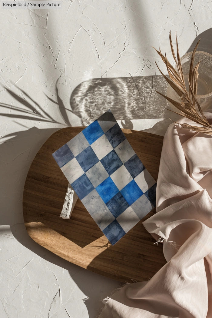 A blue and white checkered tile on a wooden surface with dried grass and beige fabric nearby.