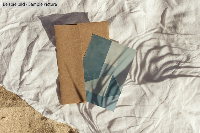 Abstract art print with geometric shapes on a textured paper, placed on a sandy surface with subtle shadows.