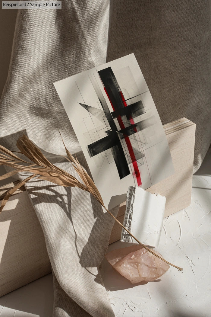 Abstract artwork with red and black streaks on paper, set against textured fabrics and stones in natural light.