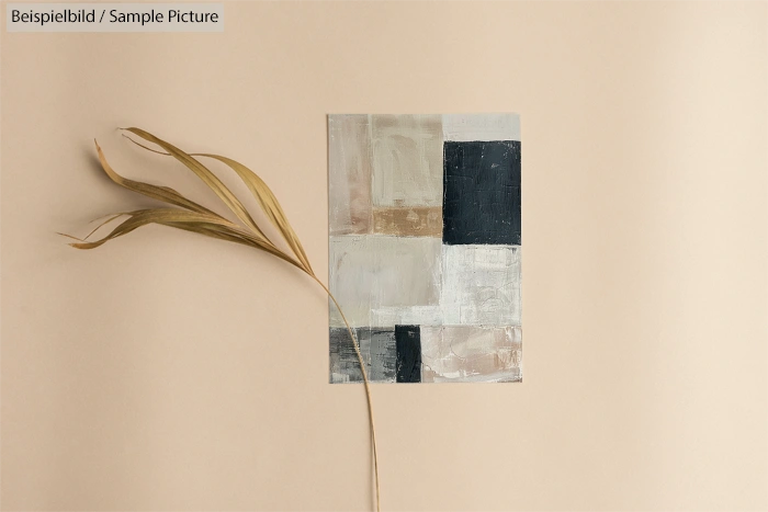 Abstract geometric painting with beige, white, black, and grey blocks, alongside a dried plant on a beige background.