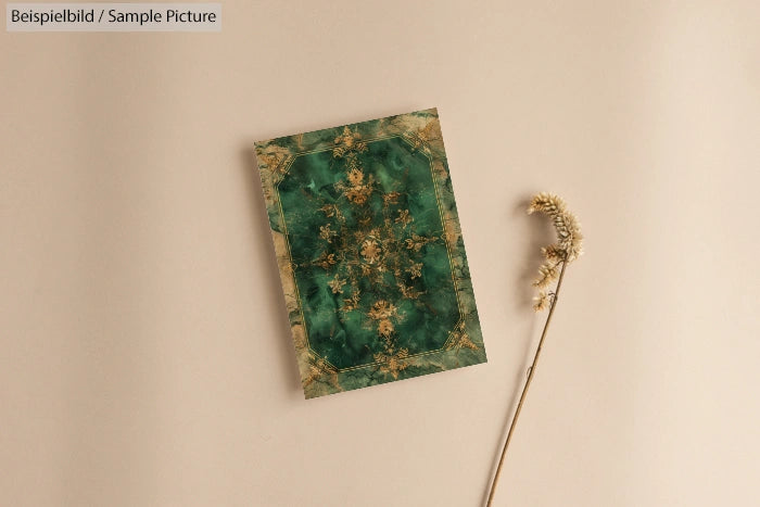 Green and gold ornate card on beige background with dried flower stem beside it.