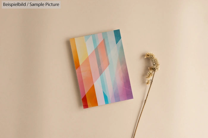 Colorful geometric pattern on a notebook cover beside a dried flower on a beige background.