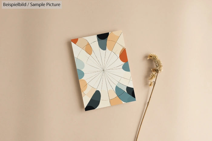 Geometric abstract artwork with colorful shapes on beige background, next to a dried flower stem.