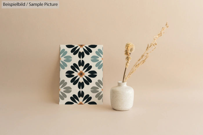 Decorative card with floral pattern next to a vase with dried flowers on a beige background.