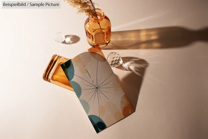 Decorative card with abstract circles and lines next to amber glass bottles on a beige surface with shadows.