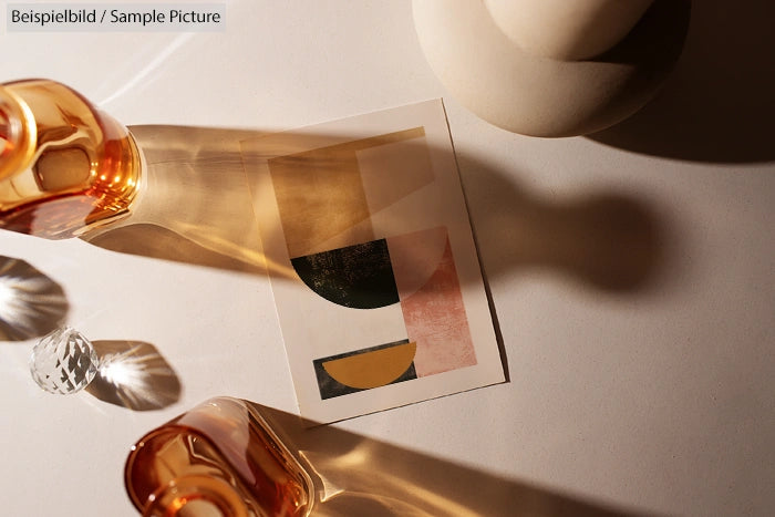 Abstract art print on table with glass shadow reflections and decorative objects in warm lighting.