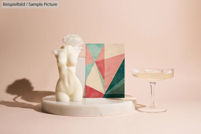 Geometric art, female torso sculpture, and glass of champagne on marble platform against peach background.