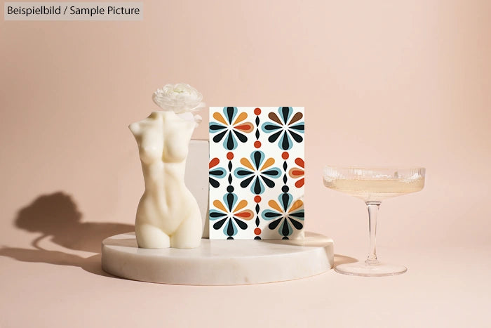 Minimalist art display with abstract vase, patterned card, and vintage glass on round marble base.