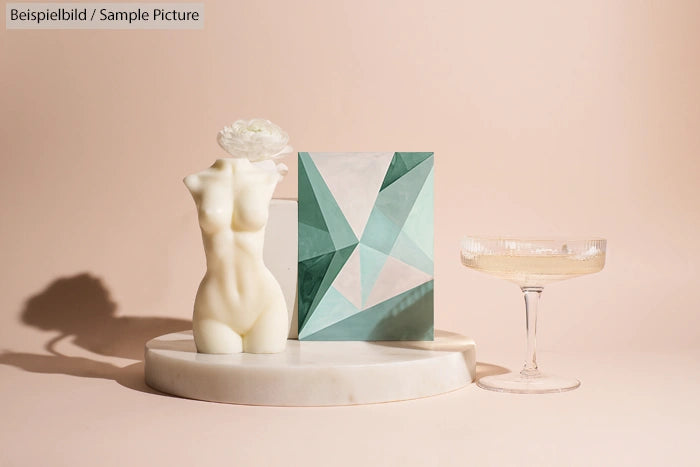 Abstract sculpture with geometric artwork and a glass on a white platform.