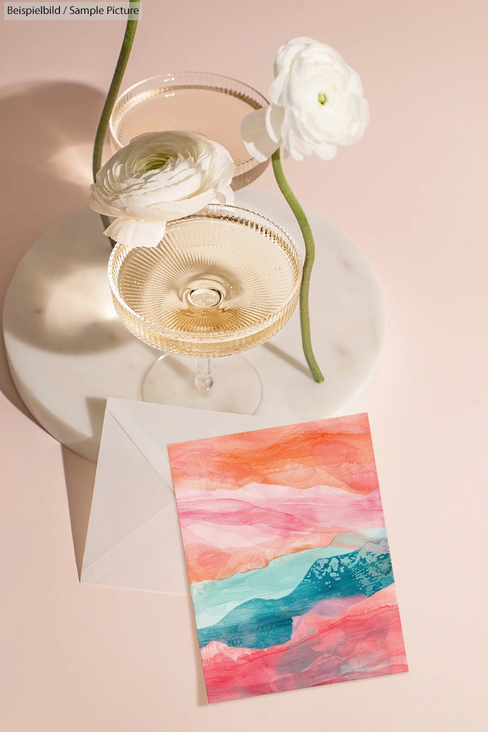 Champagne glasses and white flowers on a marble tray with a colorful abstract card on a pastel pink surface.