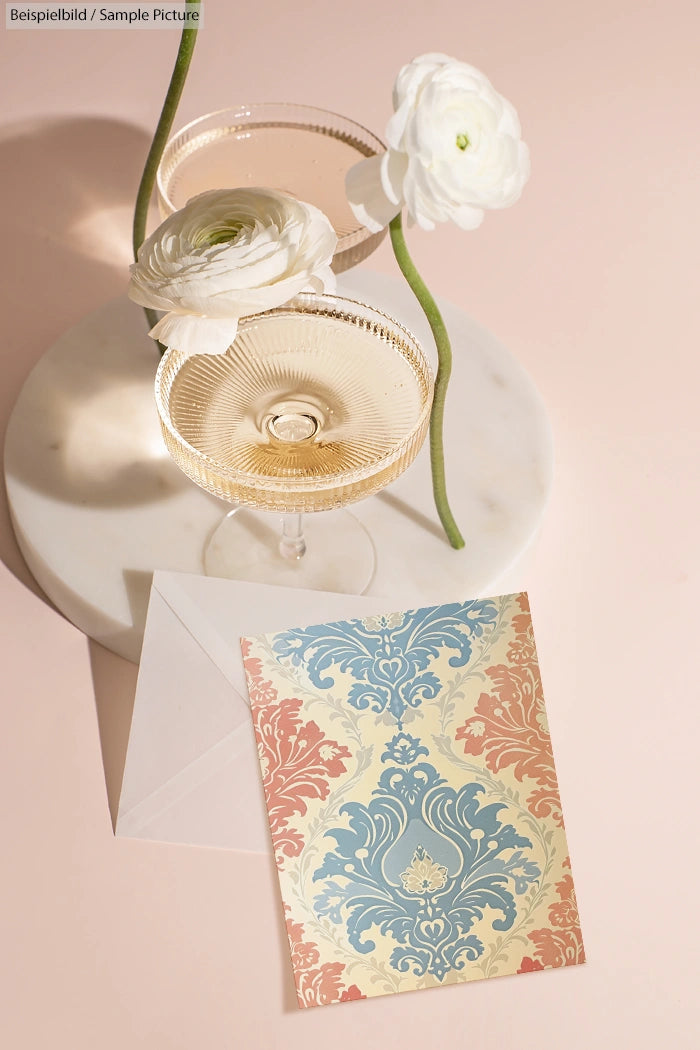 Two elegant glasses on a marble surface, with white flowers and a decorative card on a pink background.