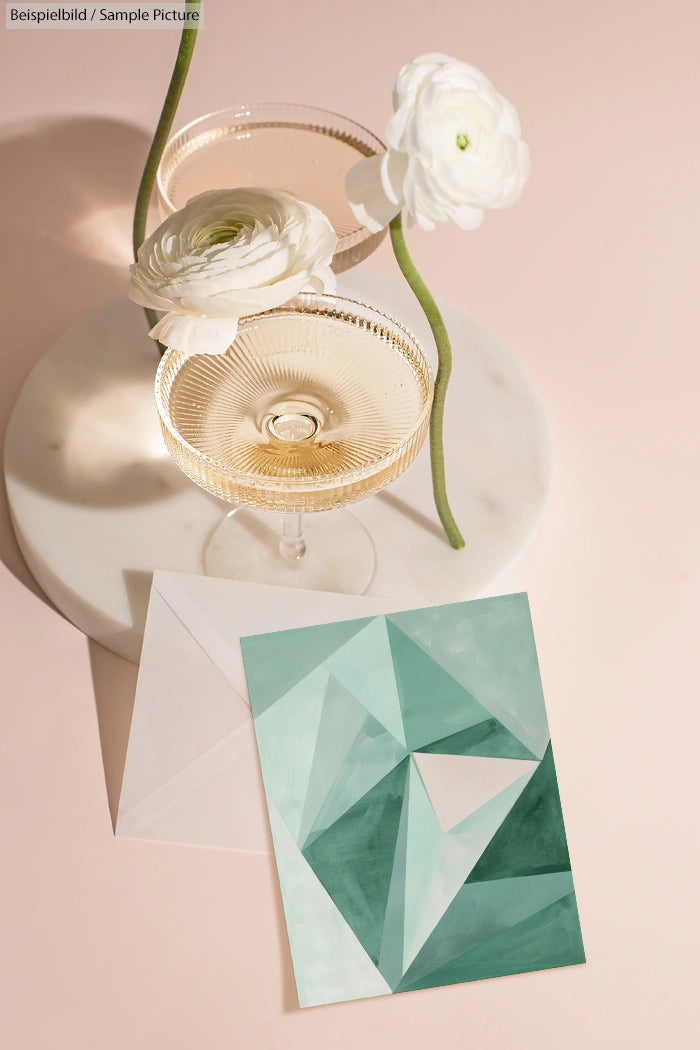 Elegant champagne glasses with white flowers and abstract geometric card on marble surface.