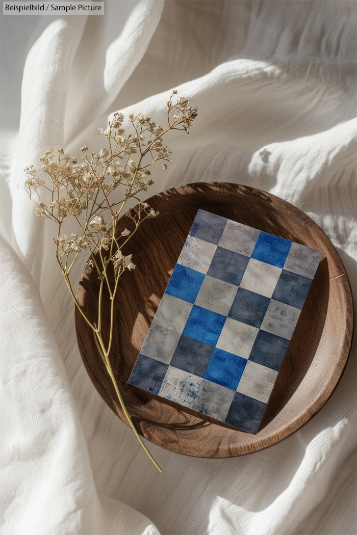 Wooden bowl with blue and white checkered card and dried flowers on soft fabric.