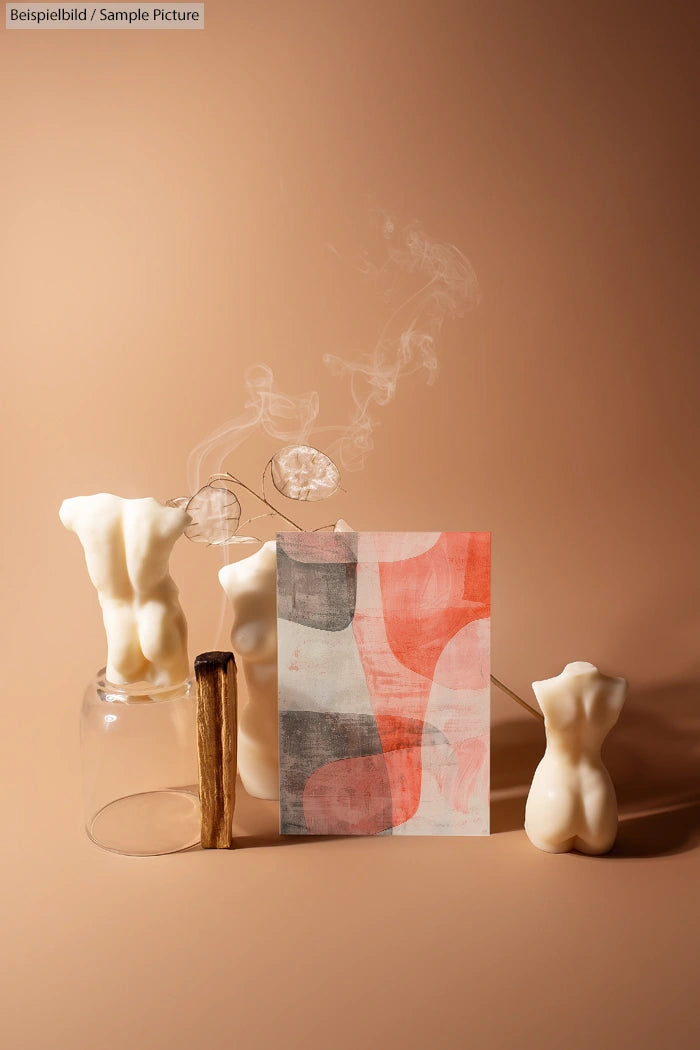 Artistic setup with abstract painting, two body-shaped candles, and incense smoke on a beige background.