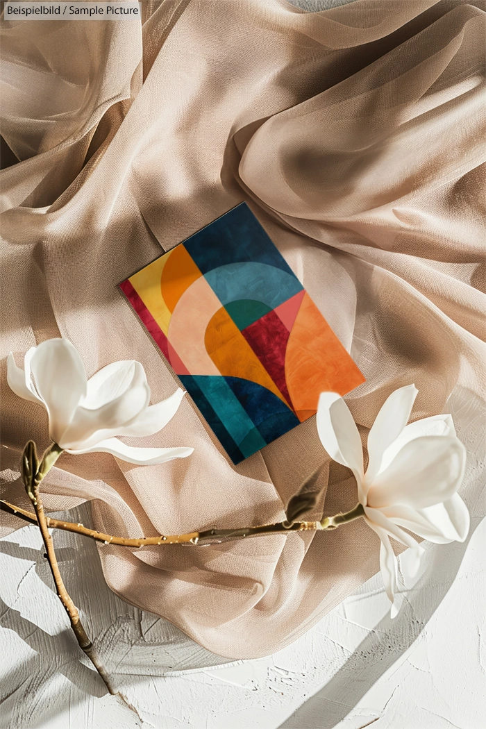 Colorful geometric painting on fabric with white magnolia flowers on a textured surface.