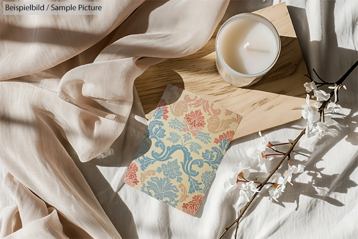 Patterned card with blue and red designs on fabric, alongside a lit white candle and decorative flowers on wooden surface.