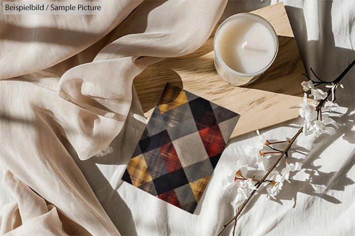 Cozy setting with a lit candle, geometric-patterned book, sheer fabric, and cherry blossoms on a wooden surface.