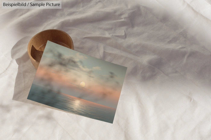 Wooden bowl and photo of serene ocean at sunset on white fabric.