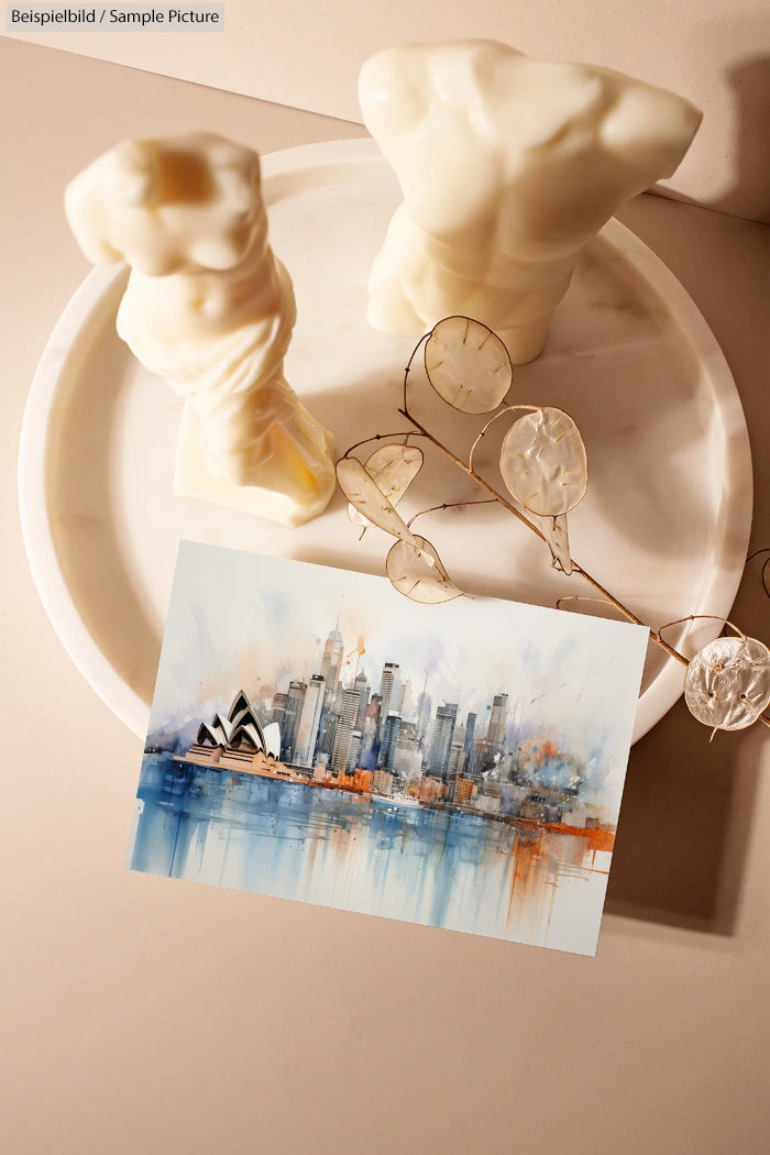 Artistic painting of a cityscape with blue and orange hues placed beside two white torso sculptures on a tray.