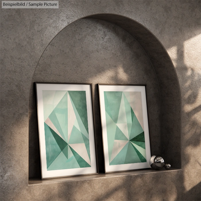 Abstract geometric art with green and gray tones in two frames on a shelf, with metallic balls as decor.