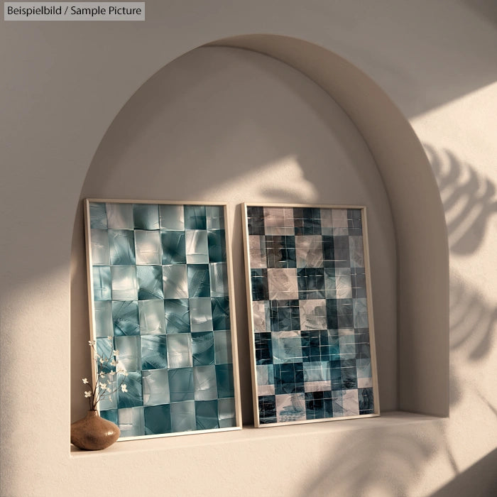 Two abstract teal and gray square pattern artworks on a curved wall shelf. Soft lighting and a small brown vase.