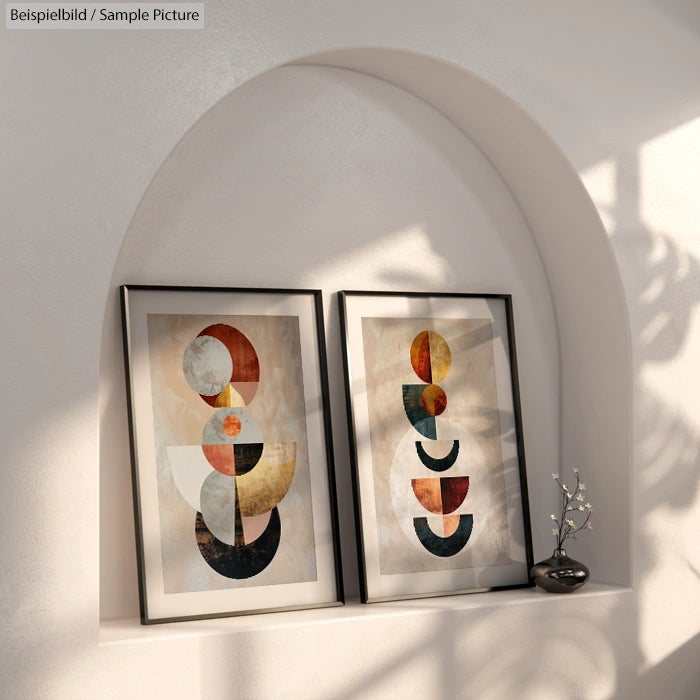 Minimalist shelf with two abstract geometric art pieces in frames, set against a white arched wall, shadow patterns visible.