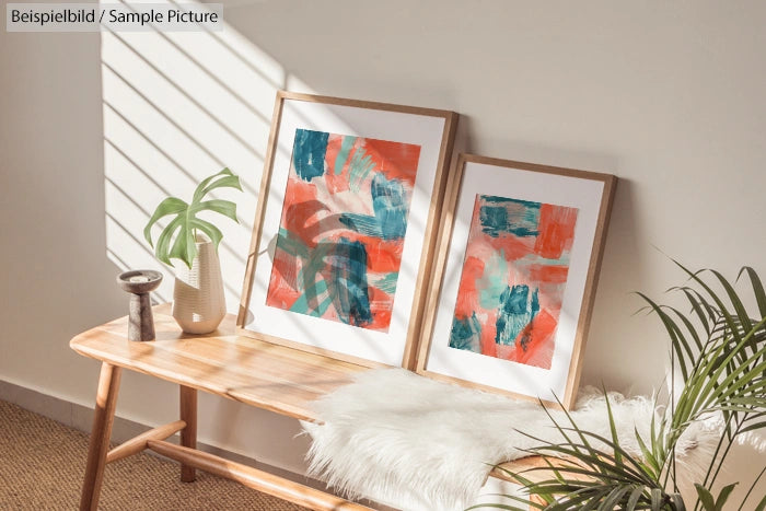 Two abstract paintings with red and teal colors on a wooden bench, next to a plant and decorative items.