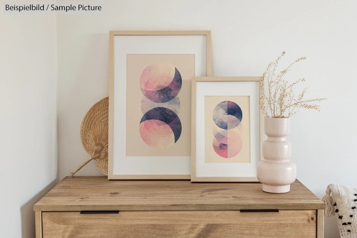 Wooden dresser with two framed abstract artworks and a ceramic vase with dried flowers.