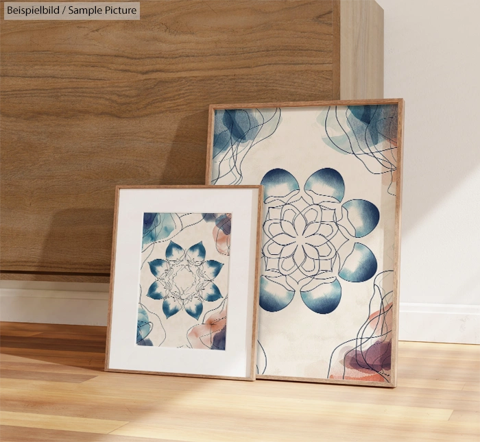 Framed abstract floral artworks on a wooden floor, depicting geometric patterns in blue and beige tones.