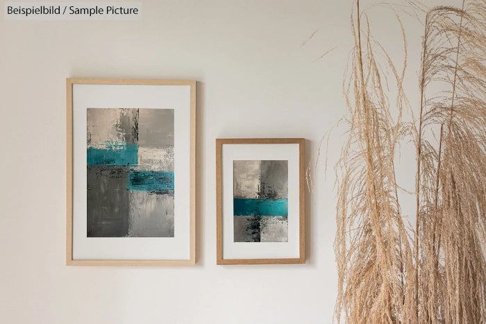 Two abstract paintings with geometric designs in blue, gray, and black, framed on a white wall next to decorative grass.