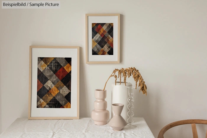 Two framed abstract quilt art pieces on a minimalist wall with ceramic vases on a table. Beige tones dominate the decor.