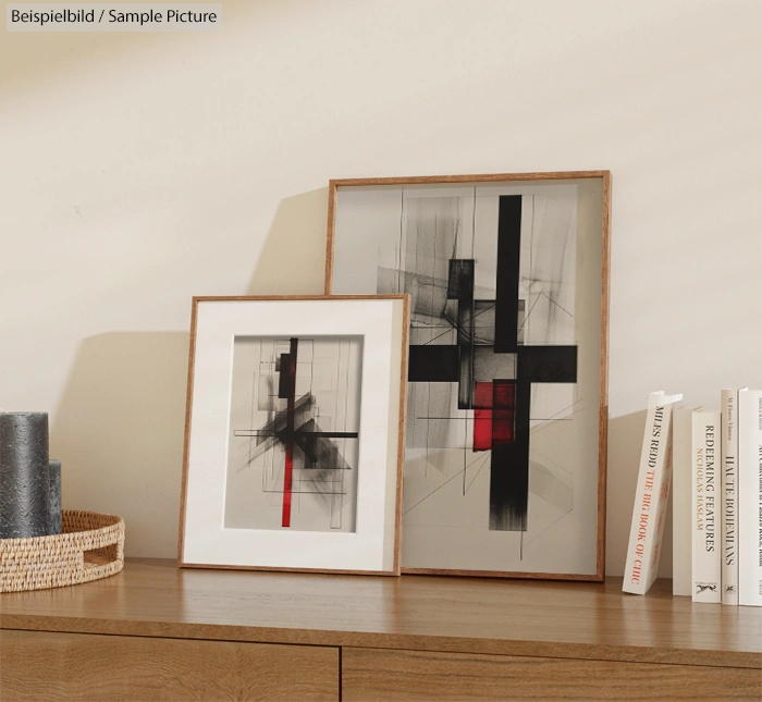 Two framed abstract artworks on shelf beside stacked books, featuring black and red lines in geometric patterns.