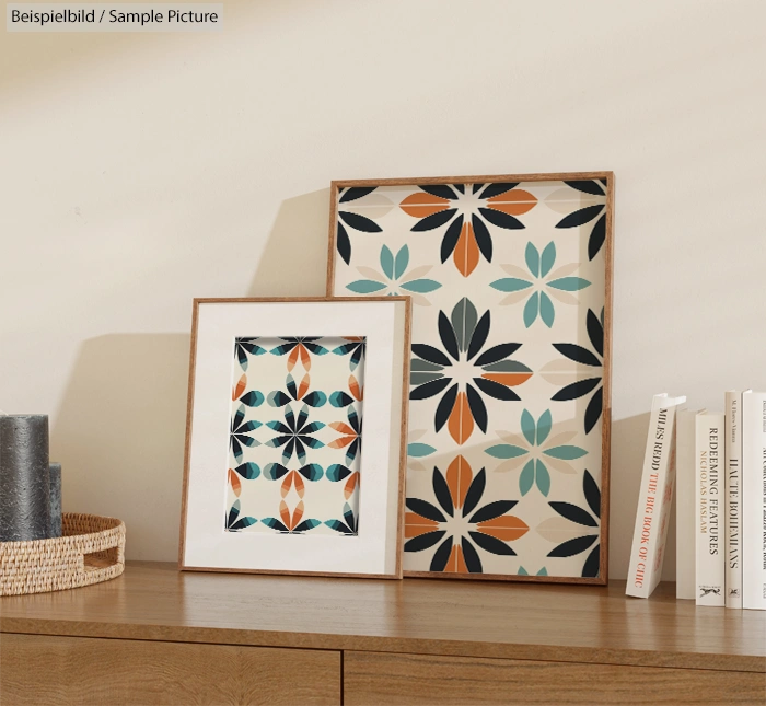 Two framed geometric floral prints on a wooden table beside books and a woven basket.