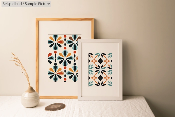 Two framed abstract flower prints on a table with a vase and dried grass.