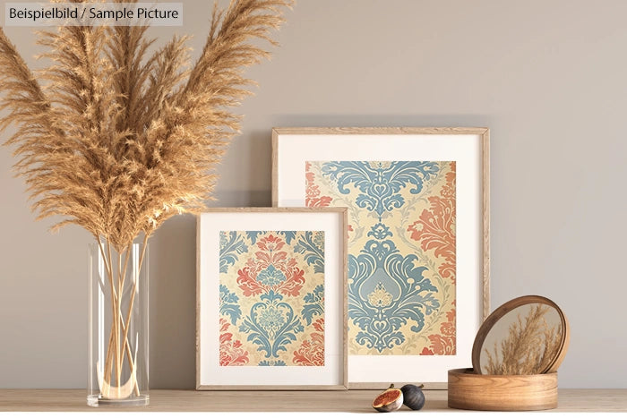 Decorative prints on a shelf with dried pampas grass in a vase and a small round mirror.