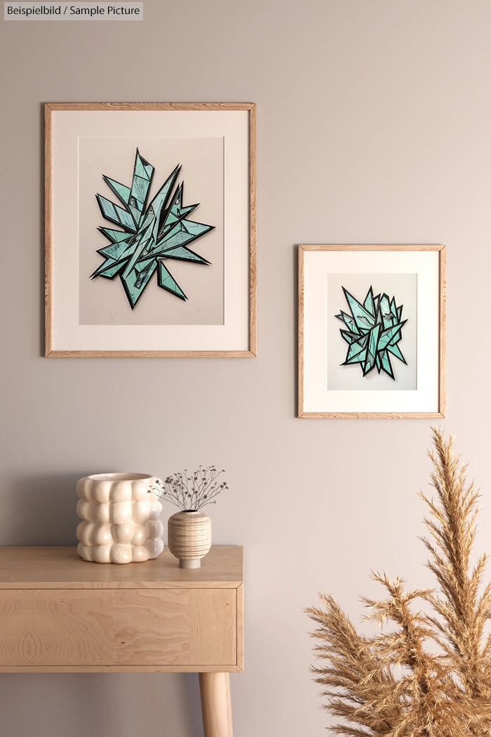 Two framed geometric art pieces on beige wall above a wooden table with white vases and dried pampas grass.