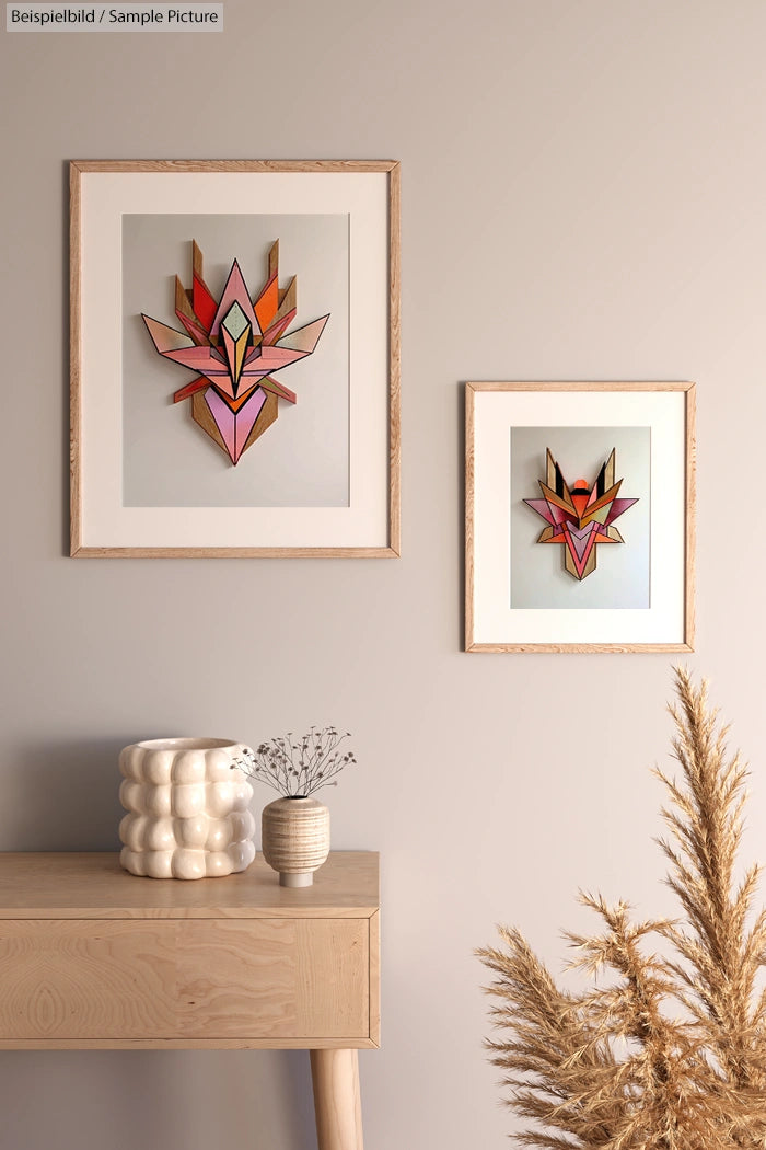 Two abstract geometric artworks in wooden frames on beige wall above a light wooden table with decorative vases.