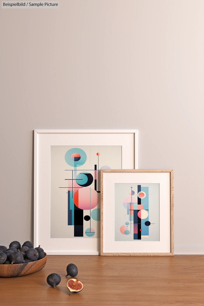 Two abstract geometric art pieces in frames; larger in white, smaller in wood, with figs in a bowl nearby.