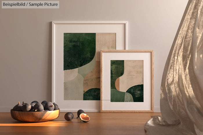 Framed abstract art with green and beige shapes on floor near figs, in a softly lit room.