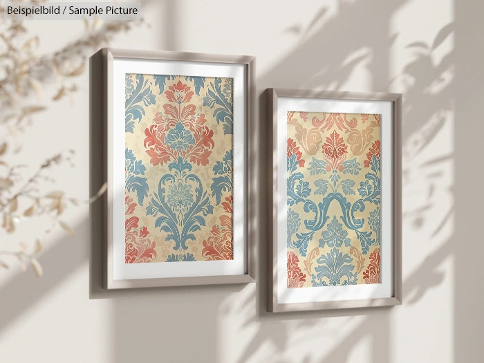 Two framed floral patterns in soft blue and coral hues, hung on a wall with sunlight and shadow play.