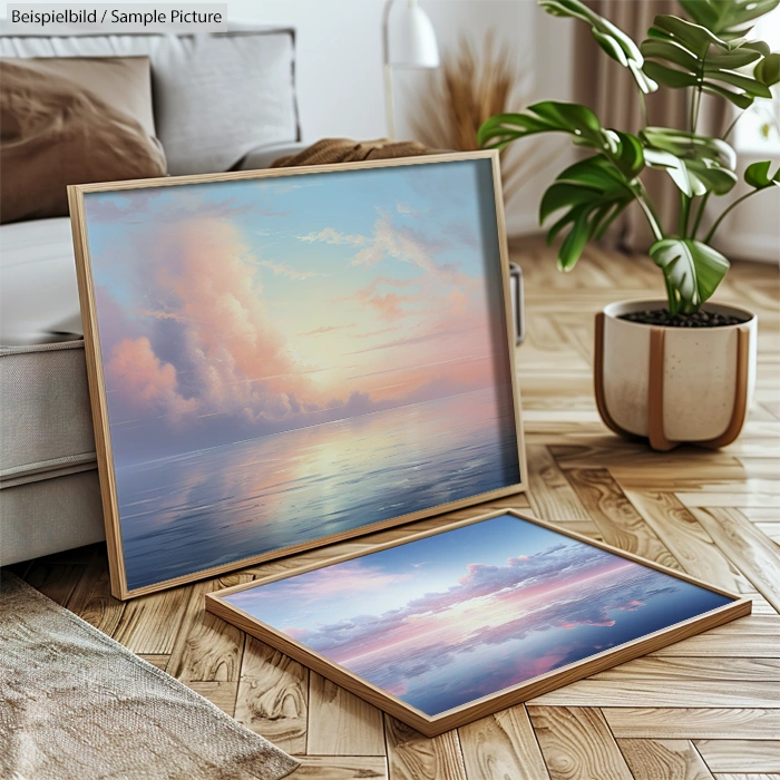 Two framed artworks of serene sunset ocean scenes on a wooden floor, beside a cozy couch and potted plant.