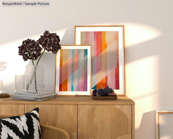 Wooden sideboard with colorful abstract art and a vase of purple flowers in a bright room.