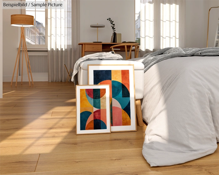 Modern bedroom with wooden floor, abstract art prints by bed, and a lamp next to large window.