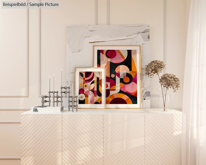 Stylish room with modern abstract art in wooden frames on a white sideboard, accompanied by candles and dried flowers.