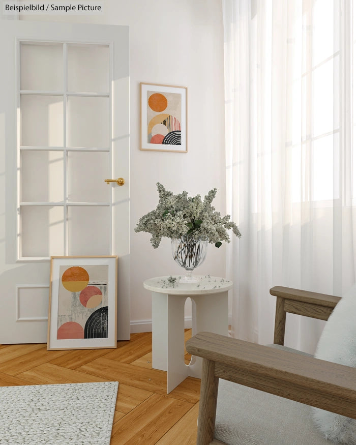 Minimalist room with abstract art, a vase of flowers on a small table, and a wooden chair beside a sunlit window.