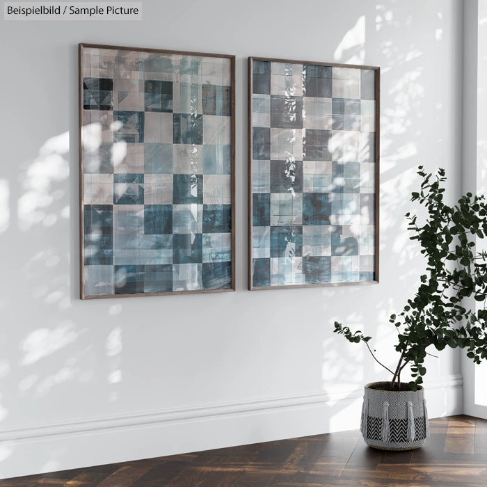 Two abstract geometric artworks with blue and gray tones in a bright room with a potted plant.