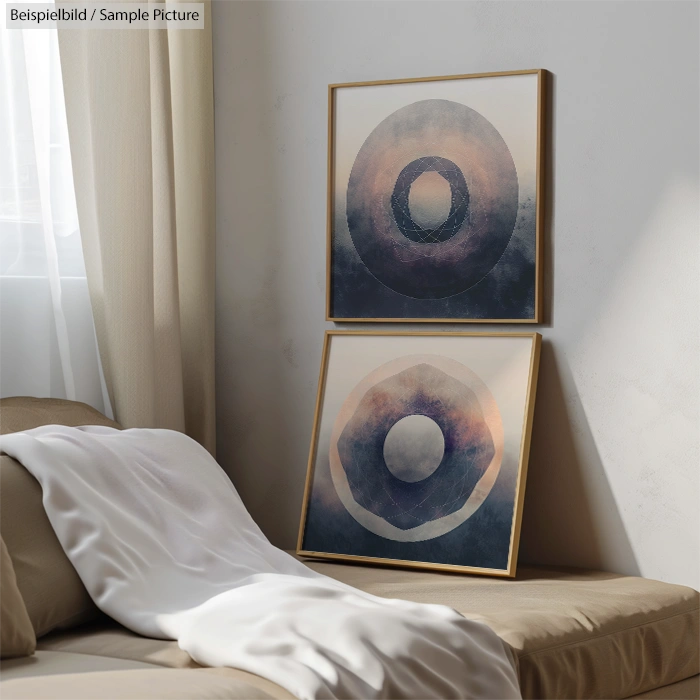 Two framed abstract paintings with circular designs on a wall above a beige sofa and white draped throw.