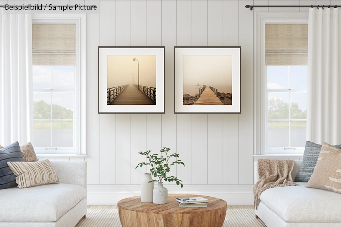 Minimalist living room with white decor, two framed sepia-toned pier photos, and wooden coffee table.