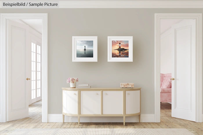 Minimalist living room with light gray walls, two framed artworks, a white cabinet, and a glimpse of a pink chair.