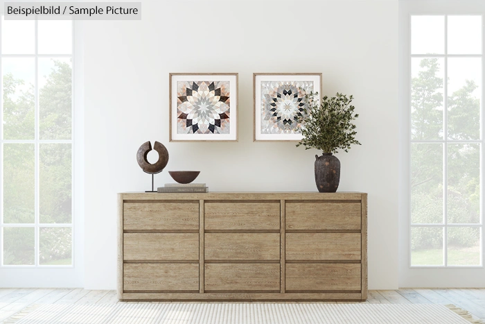 Minimalist room with wooden sideboard, two geometric art pieces, and potted plant against large windows.